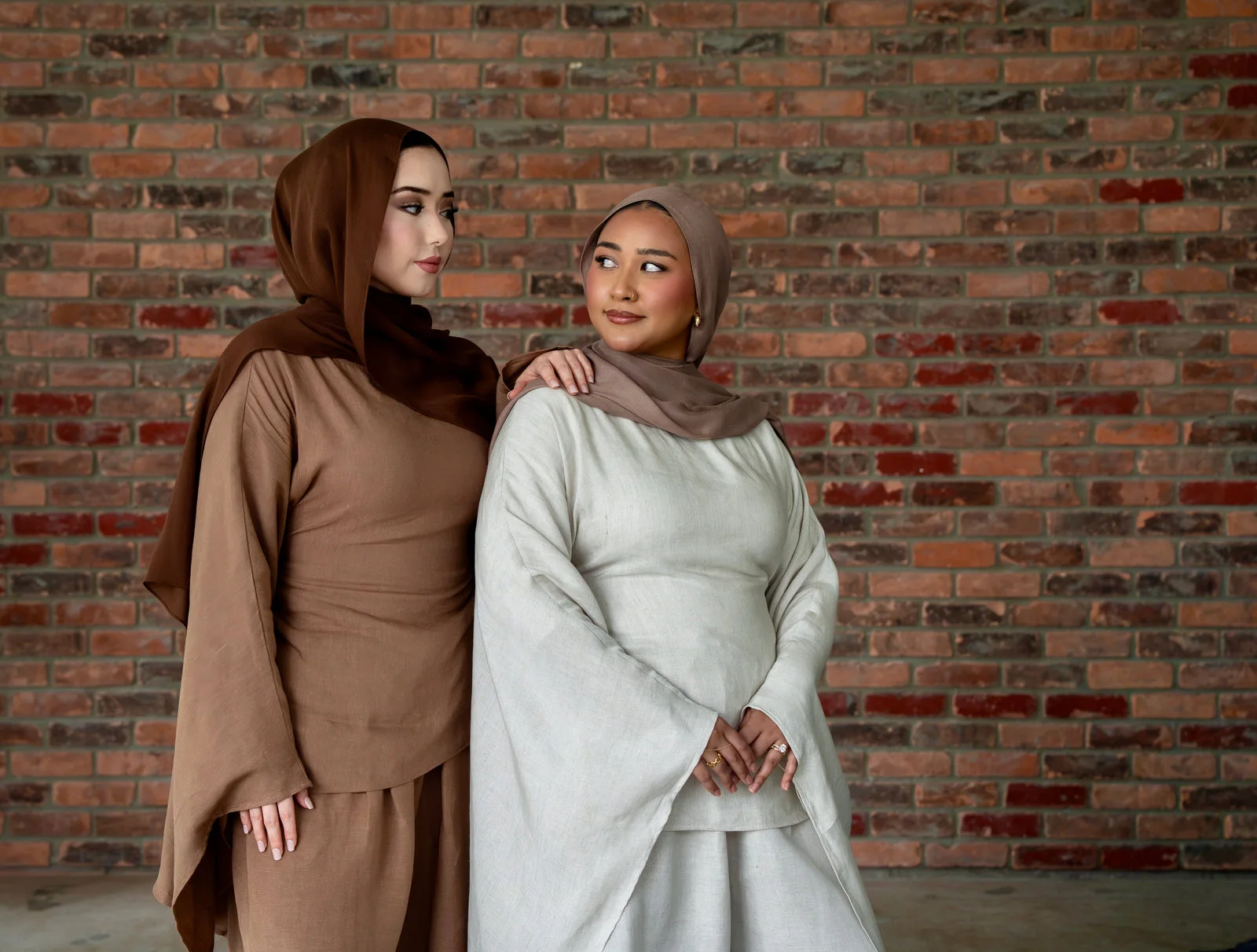 Two models wearing Mondo The Label linen sets in brown and sage against a brick wall